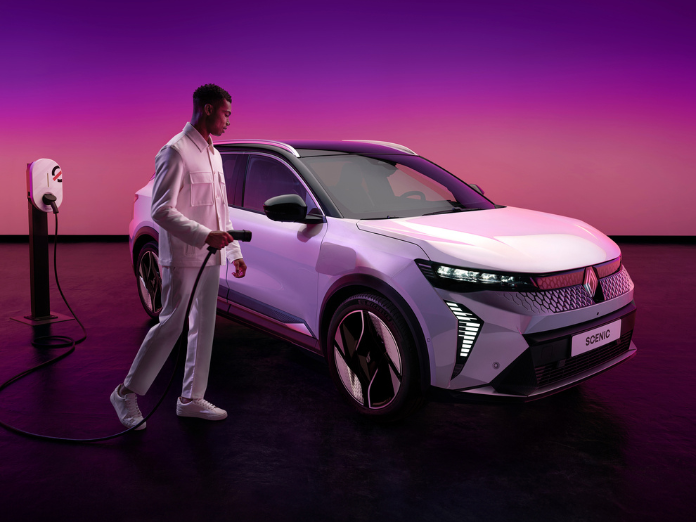 Man wearing white trousers and shirt holding mobilize charger next to white renault scenic