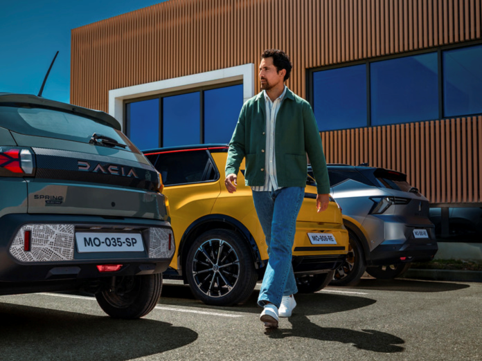 Man In Green Jacket and jeans walking across car park with Dacia Spring R5 R4