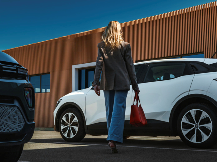 White Renault Scenic with lady in wide leg jeans taupe jacket and red bag walking towards car