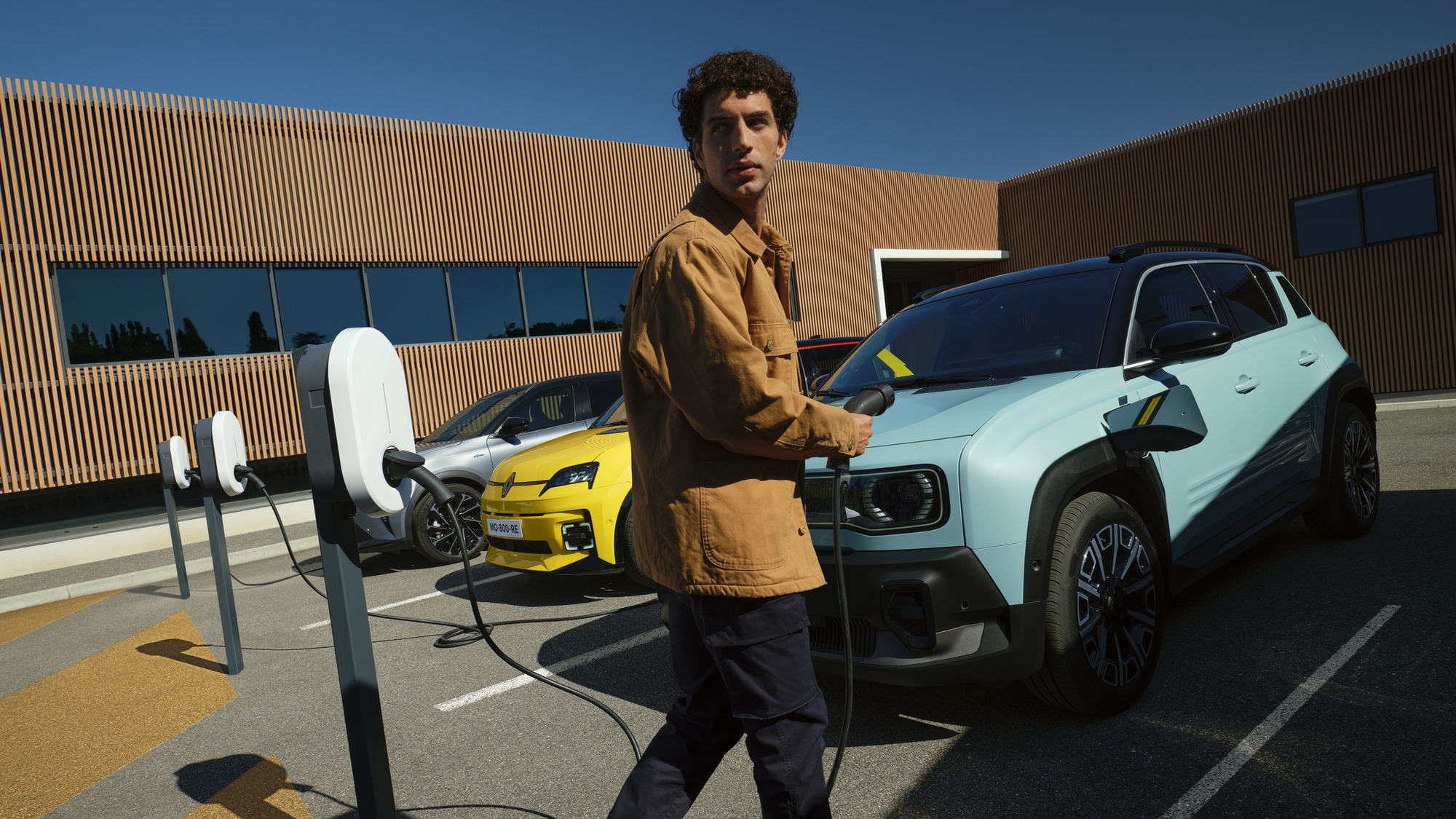 Man holding charger with three cars in background 