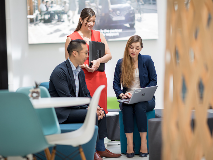 Two female and one male in business attire looking at a laptop screen sitting in an office environment